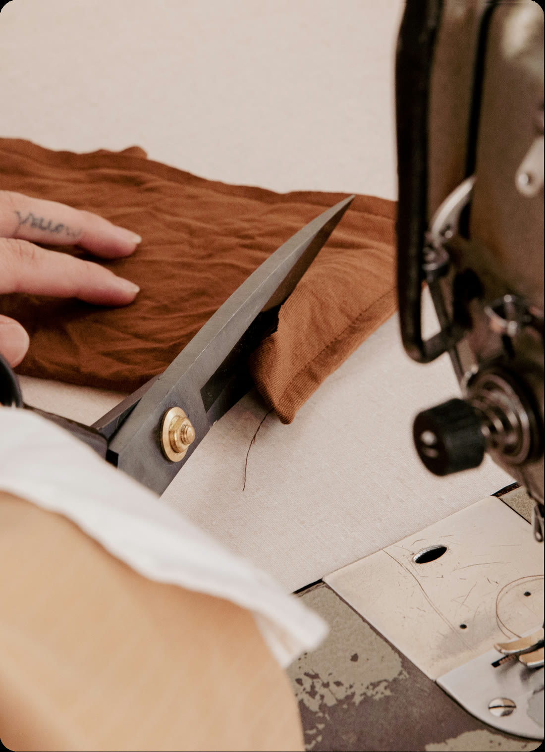 A tailor cutting fabric beside a sewing machine